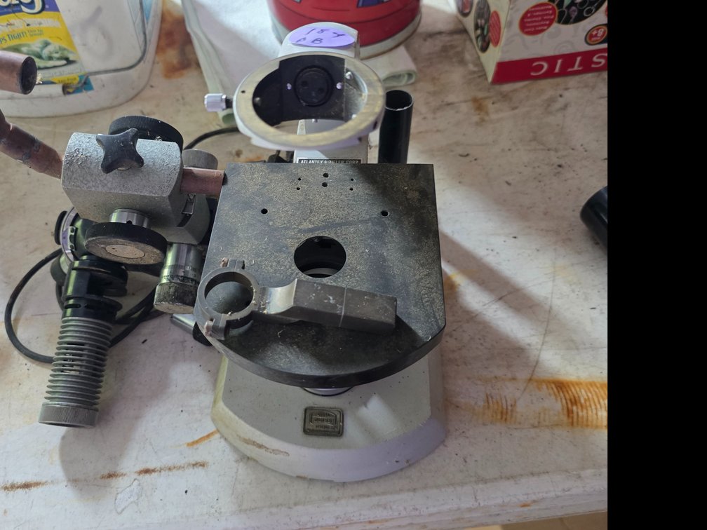 Stereomicroscope or measuring microscope assembly with a heavy metal stand, circular stage, and a detached optical head/arm. Microscope: Features a heavy grey cast metal base