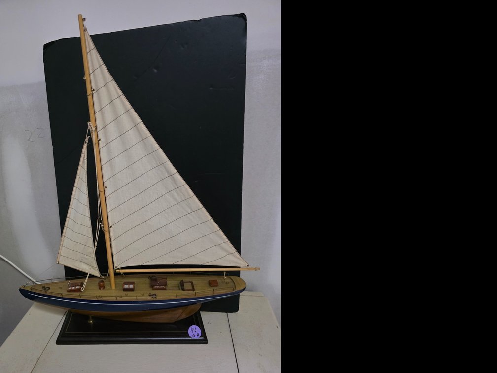 Decorative wooden sailboat model featuring beige fabric sails and a dark blue and wood-tone hull mounted on a rectangular display base.