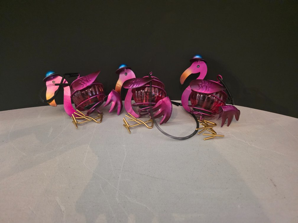 set of decorative metal and glass pink flamingo solar garden or tabletop lights featuring vibrant gradient finishes, curved necks with black and yellow accents, and open-work caged glass bodies.