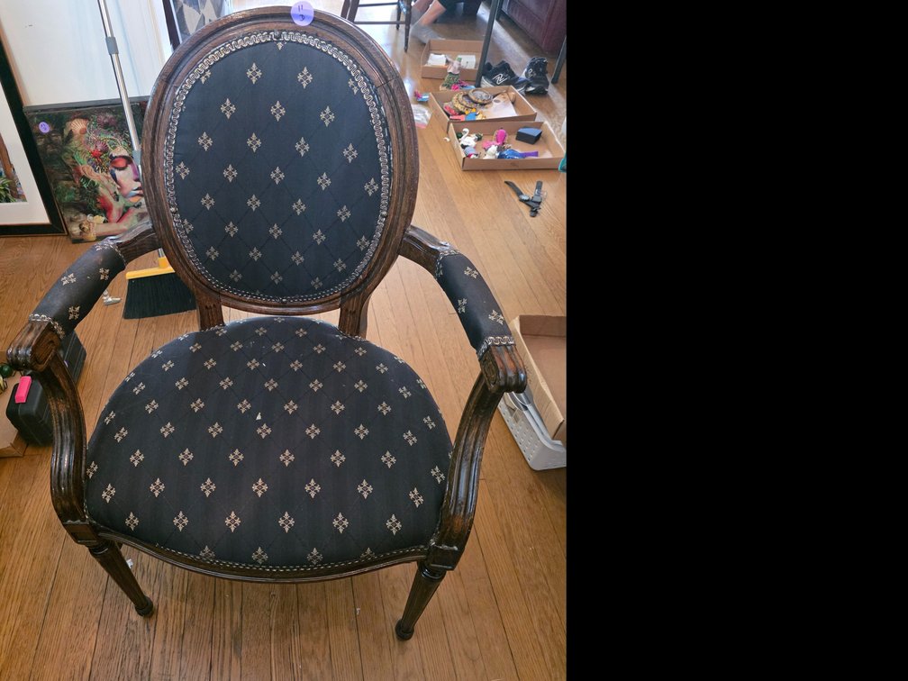 French Louis XVI-style carved wo, featuring a round medallion back, upholstered armrests, and decorative nailhead trim.