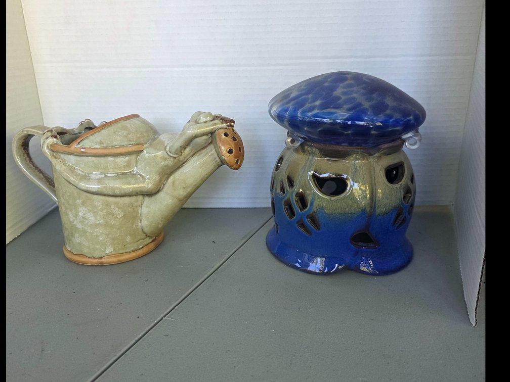 Charming ceramic watering can features a delightful sculpted frog lounging along the spout with a speckled green glaze. blue and tan glazed ceramic pottery piece