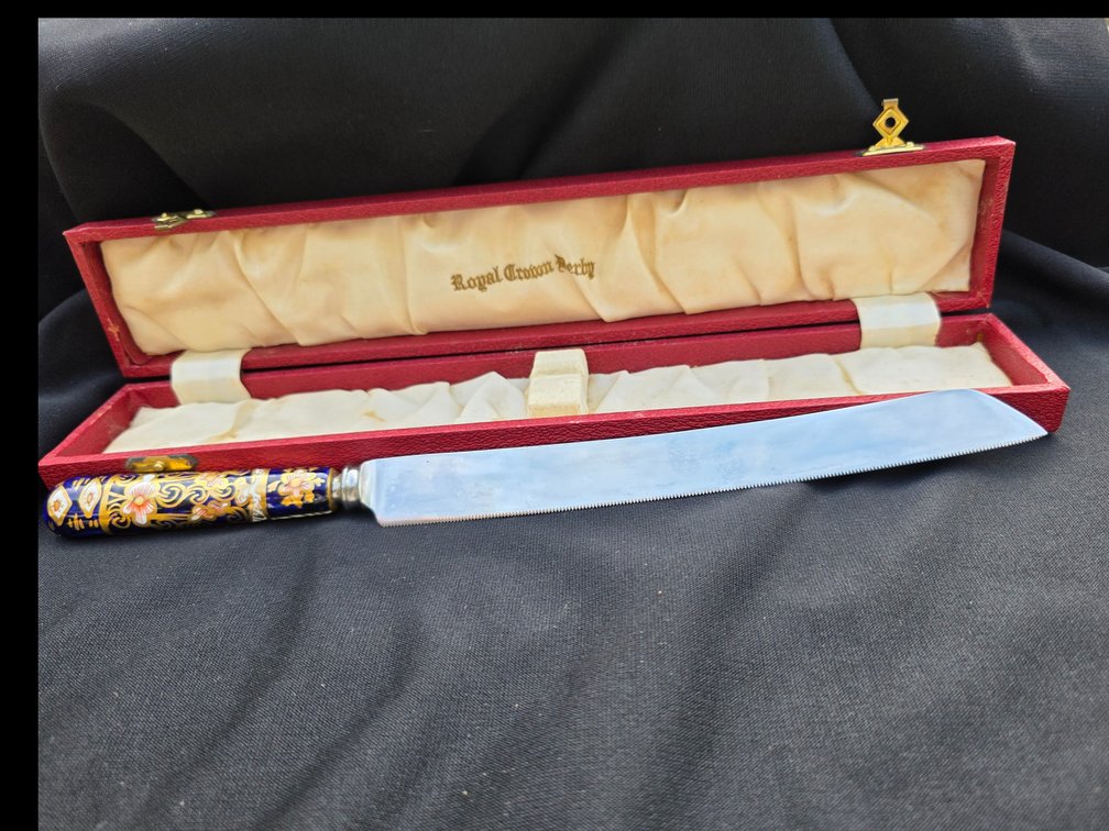 Vintage Royal Crown Derby bread or cake knife featuring an ornate porcelain handle with a traditional Imari-style floral and gilded pattern, housed in a fitted presentation box.