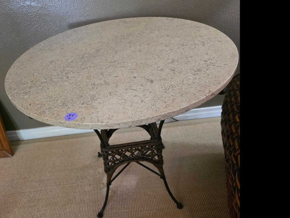 Round stone-top table featuring a black wrought iron base with scrollwork and a woven center accent.
