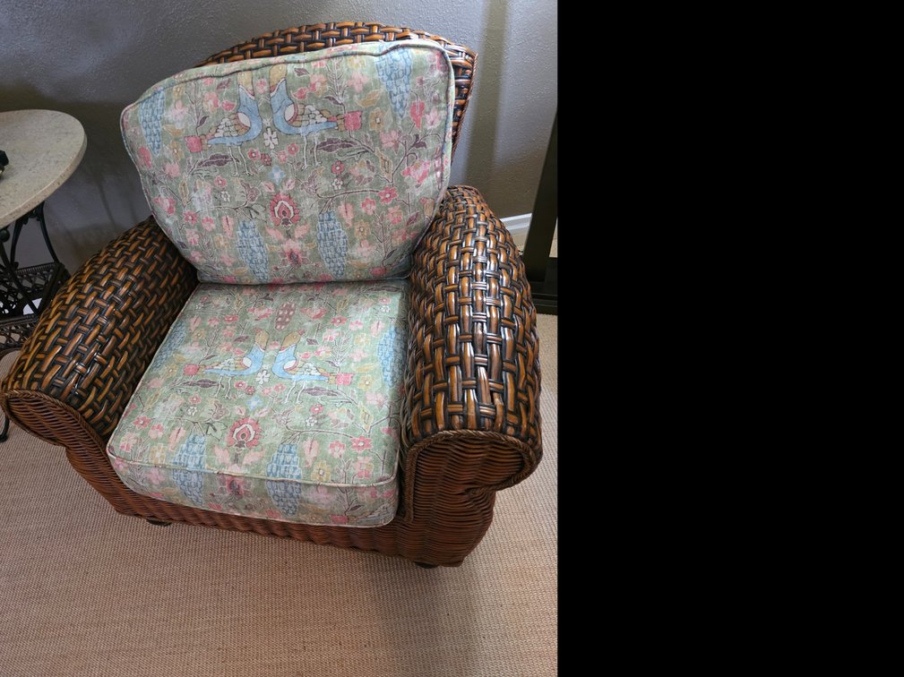 Vintage brown woven wicker and rattan club armchair featuring rolled arms and floral print cushions,