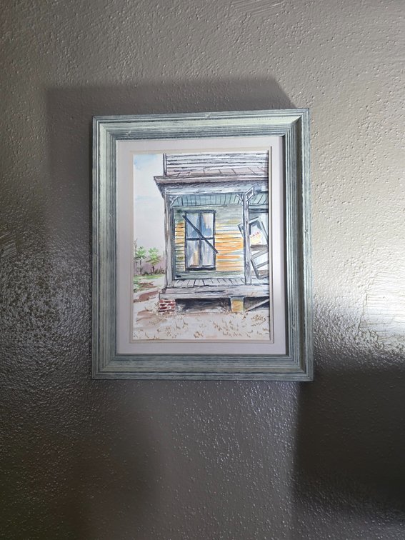 Framed watercolor painting shows a weathered, rustic Southern porch or old house
