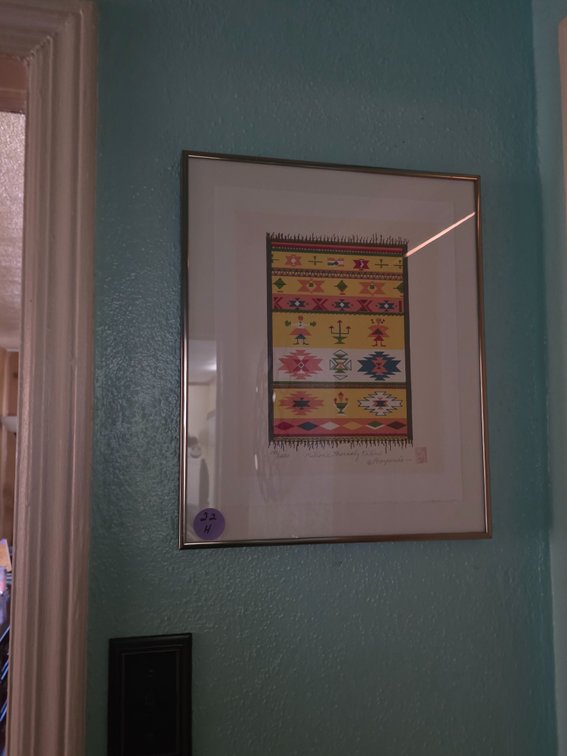Framed art print depicting a vibrant, geometric tribal kilim rug with horizontal bands of colorful symbols, figures, and patterns.