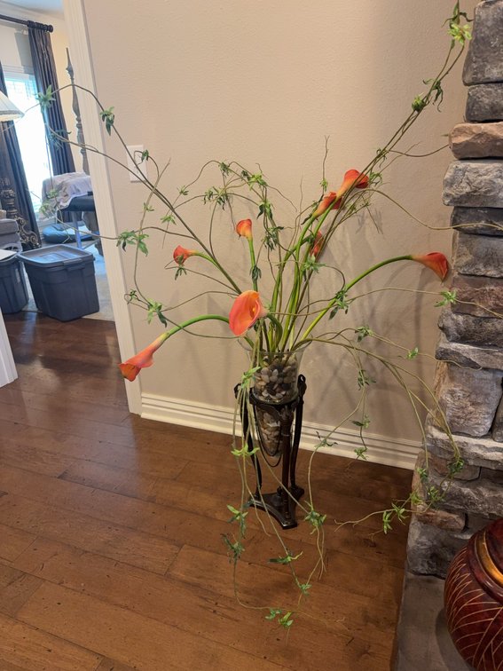 Tall Glass Vase With Mixed Stones and Orange Calla Lilies On Ornate Metal Stand
