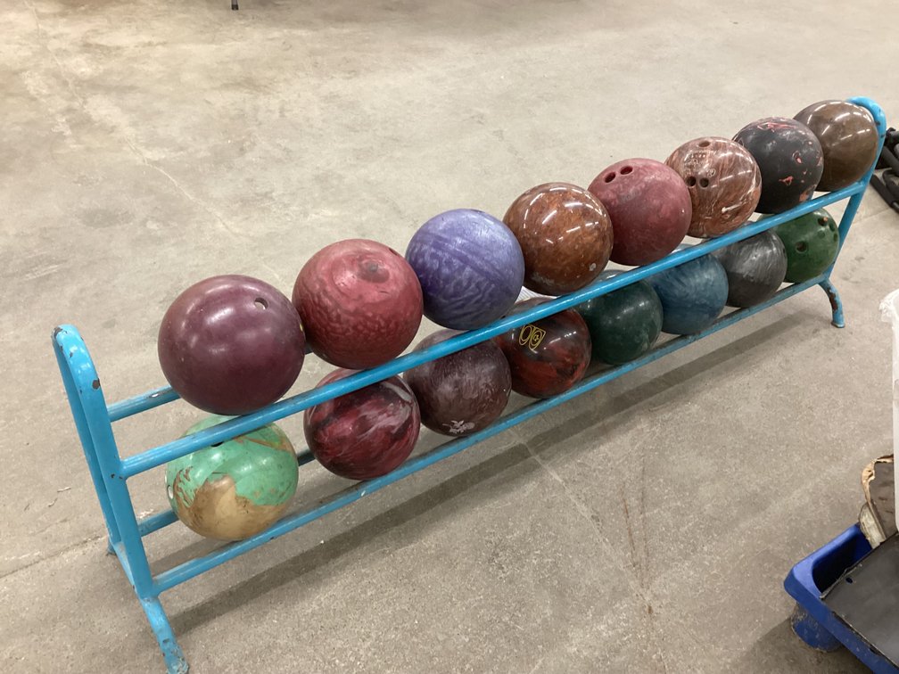 Rack of bowling balls and box of magazines. 
