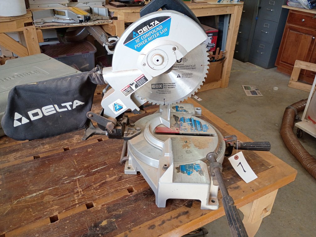 Delta 10-inch compound miter saw equipped with a Delta-branded dust collection bag and a multi-tooth carbide saw blade
