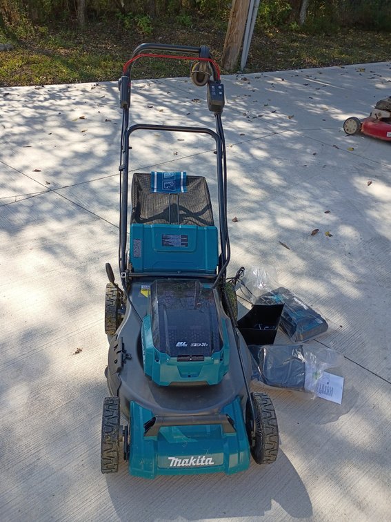 teal-and-black Makita 36V (18V X2) LXT Brushless Cordless Self-Propelled Lawn Mower (such as the Makita XML08 or DLM series) with its grass catcher bag, battery charger, and manuals. Tested and works