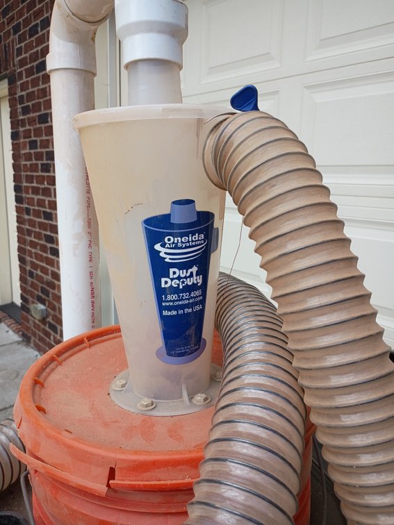 an Oneida Air Systems Dust Deputy Cyclone Separator mounted onto a collection bucket and connected to a shop vacuum hose and PVC piping.
